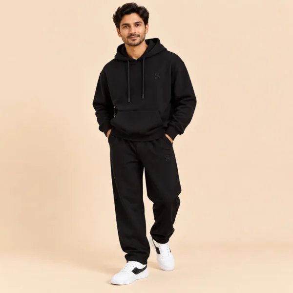 Man wearing the Sportlux Plus black 350 GSM fleece hoodie co-ord set, relaxed hoodie and straight leg trousers with tonal embroidered S monogram, full length view