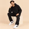 Man seated wearing the Sportlux Plus black 350 GSM fleece hoodie co-ord set with white trainers