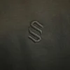 Close-up of the tonal black embroidered S monogram on the Sportlux Plus black fleece hoodie