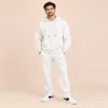 Man wearing the Sportlux Plus cream 350 GSM fleece hoodie co-ord set, relaxed hoodie and straight leg trousers with tonal embroidered S monogram, full length view