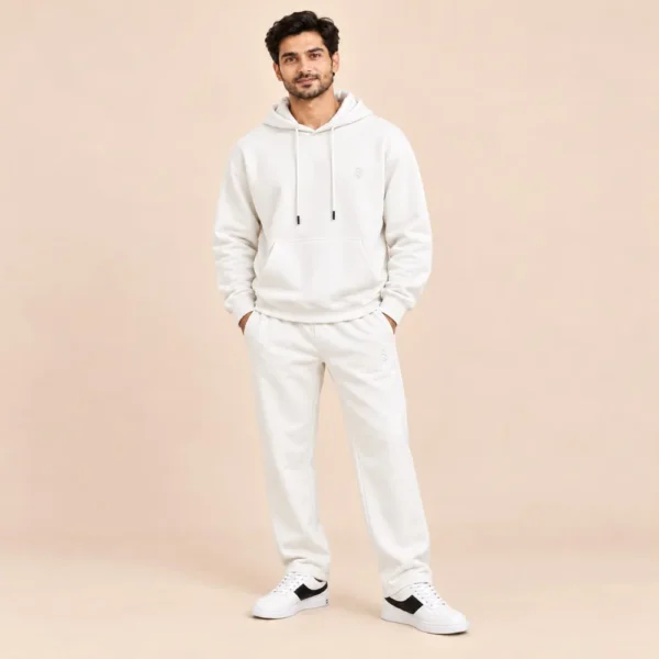 Man wearing the Sportlux Plus cream 350 GSM fleece hoodie co-ord set, relaxed hoodie and straight leg trousers with tonal embroidered S monogram, full length view