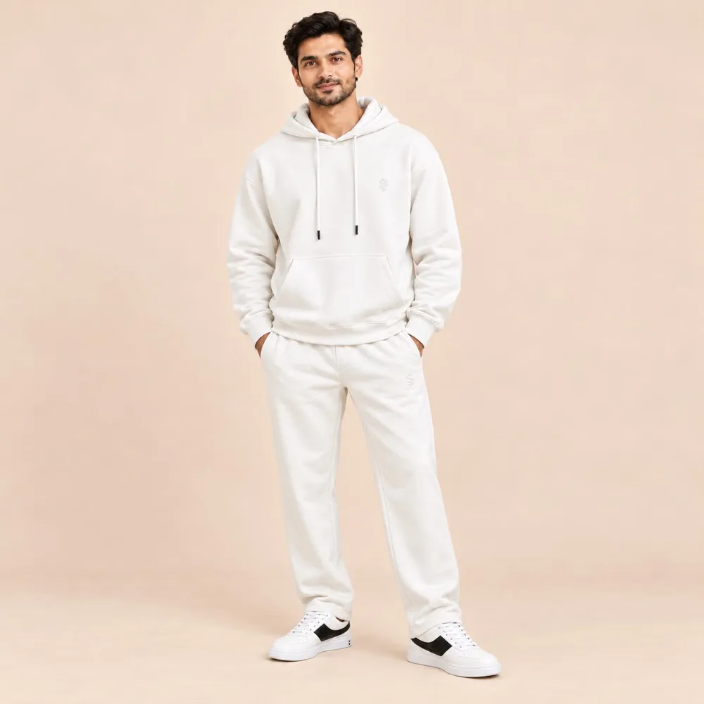 Man wearing the Sportlux Plus cream 350 GSM fleece hoodie co-ord set, relaxed hoodie and straight leg trousers with tonal embroidered S monogram, full length view