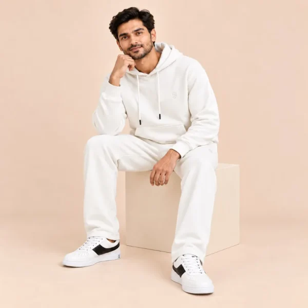 Man seated wearing the Sportlux Plus cream 350 GSM fleece hoodie co-ord set with white trainers