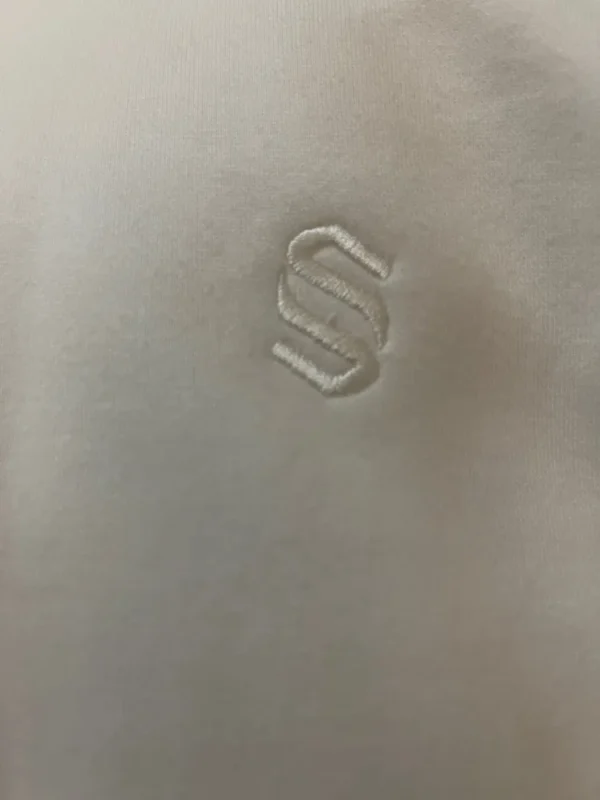 Close-up of the tonal cream embroidered S monogram on the Sportlux Plus cream fleece hoodie