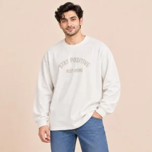 Man wearing the Sportlux Plus off-white oversized drop shoulder full sleeve t-shirt with tonal STAY POSITIVE KEEP GOING high density screen print and blue jeans, front view